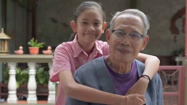 照片上 可爱的泰国小孙女在摆出姿势 看着镜头在家里时 拥抱着年长健康的祖父 有两代人的家庭中的团结 健康的生活方式 — 图库视频影像