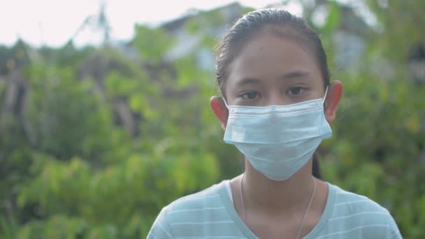 カメラを見て田舎の村に滞在するアジアの愛らしい女性のティーンエイジャーの肖像画 Covid 19流行中の安全のために練習保護マスクで不幸なタイの女の子 — ストック動画