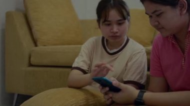 İki Asyalı genç kız kardeş yerde oturmuş sosyal videoları izliyor ve evde cep telefonlarından internette birlikte sörf yapıyorlar. Asyalı kardeşlerin yaşam tarzı.