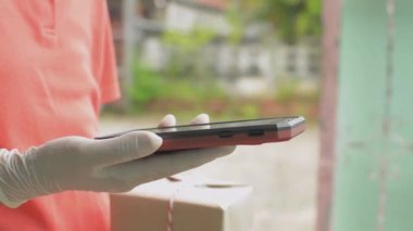 Bir teslimatçı kadından karton bir kutu al ve ödeme için akıllı telefonlu QR kod taramasını kullan. Mobil cihazda taranıyor ve ödeme yapılıyor.
