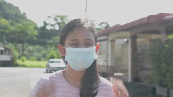 かなり長い髪アジアの女性のティーンエイジャーは 彼女の家の外に立っている間 保護顔マスクを脱いで カジュアルな服装のタイ人女の子の肖像が深く呼吸し カメラを見て 回復し 正常に戻る — ストック動画