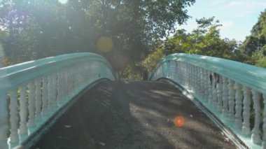 Kamu parkında sabah güneşinin altında doğal bir göleti geçen eski beton köprüde koşan bir kadının arka görüntüsü. Havadan geriye doğru atış. Kirlilikten arındırılmış ortamda egzersiz.