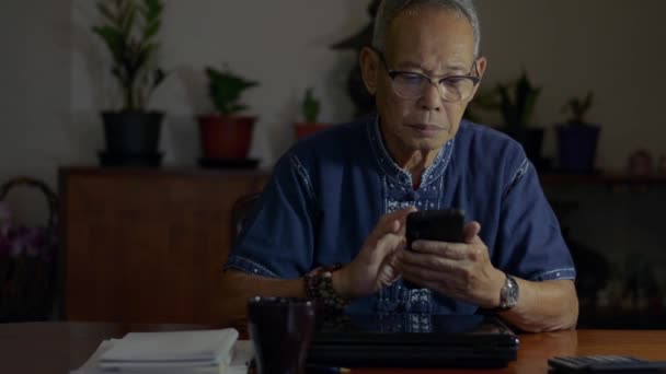 亚洲资深人士行政人员持有现代智能手机发短信在办公室在夜间 年长的商人使用有用的移动应用程序为企业管理组织服务 迟到了在家工作 — 图库视频影像