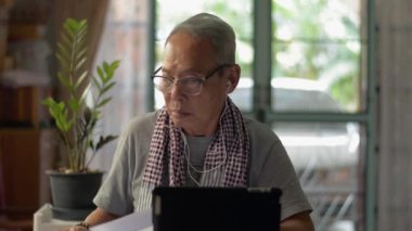 Evdeki dijital cihazda video görüntülü arama ile şirket toplantısı için günlük kıyafet hazırlayan Asyalı üst düzey erkek yönetici danışmanı. İş için uzaklık iletişim teknolojisi.