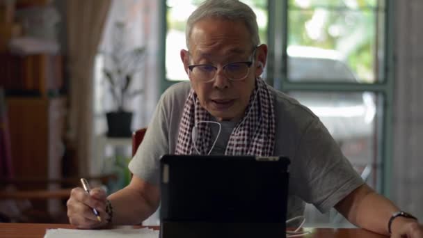 デジタルタブレットでオンラインレッスンを学び 自宅で論文を書くためのビデオチュートリアルを見てカジュアルなドレスでアジアの高齢者の祖父 高齢者の教育技術 家の隔離 — ストック動画