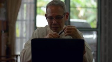 Geleneksel giyimli Asyalı üst düzey erkek iş danışmanı evdeki bilgisayar bilgisayarında video görüntülü Webinar 'ı olan şirket çalışanı ile konuşuyor. Uzaklık iletişim teknolojisi. Evden çalış..