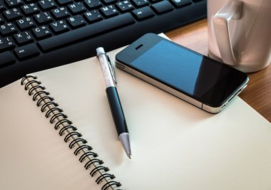 Pen on notebook with computer keyboard, and cell phone