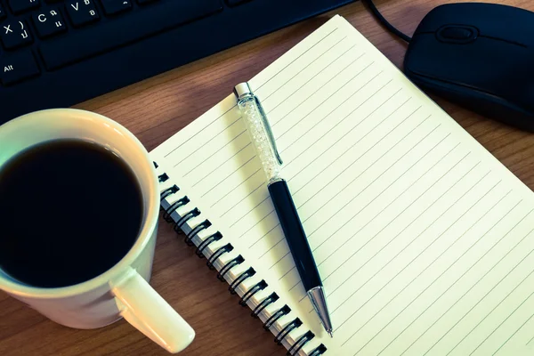 Pen on notebook with computer keyboard, mouse and a cup of coffe