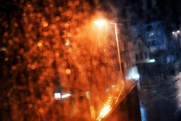 Rain drops on the window with dark streets outside and street lights shining — Stock Photo, Image