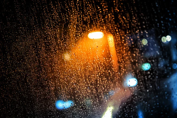 Regen druppels op het venster met donkere straten buiten en straat verlichting schijnt — Stockfoto