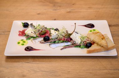 Kaliteli deniz mahsulleri sardalya, peynir, zeytin, lahanalar ve kırsal ahşap restoran masasında sanatsal soslu beyaz bir tabakta kızarmış ekmek ile başlar..