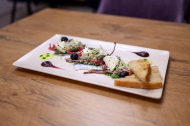 Kaliteli deniz mahsulleri sardalya, peynir, zeytin, lahanalar ve kırsal ahşap restoran masasında sanatsal soslu beyaz bir tabakta kızarmış ekmek ile başlar..