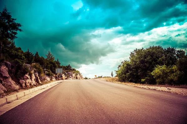 Longa estrada sem fim no campo sem tráfego com nuvens dramáticas — Fotografia de Stock
