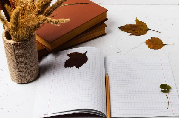 Notebook with a bookmark made of four-leaf clover on the background of an autumn bouquet and leaves  Selective focus.