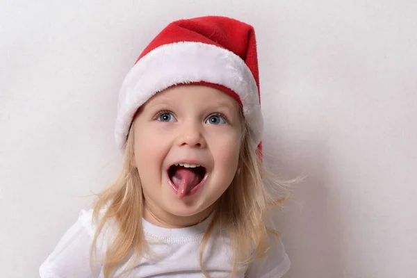 一个戴着一顶白色背景圣诞老人帽的小孩 他的舌头伸出来 图库图片