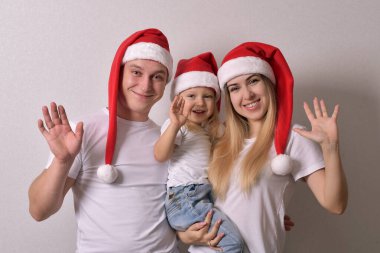 Anne, baba ve bebek Noel Baba şapkası takıp el sallıyorlar.