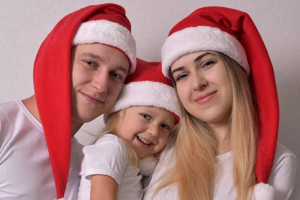 Anne, baba ve bebek Noel Baba şapkası takıyor.