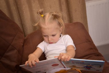 Kanepede oturmuş kitap okuyan ciddi küçük bir kız.