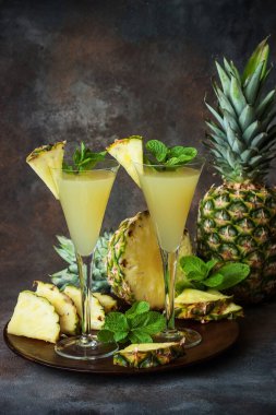 İki bardakta taze sıkılmış ananas suyu ve renkli arka planda olgun ananas.