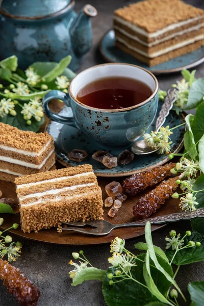 Slice of layered honey cake on plate with cup of tea, selective focus with shallow depth of field