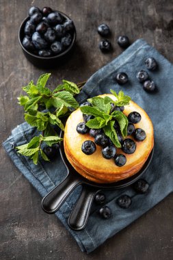 Yaban mersinli krep ve nane yaprağıyla küçük bir tavada koyu arka planda, üst manzara