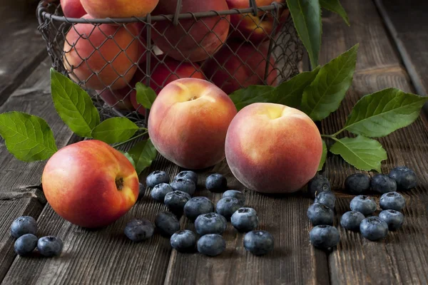 Verse perziken en nectarines met groene bladeren in een mand op een houten bord — Stockfoto