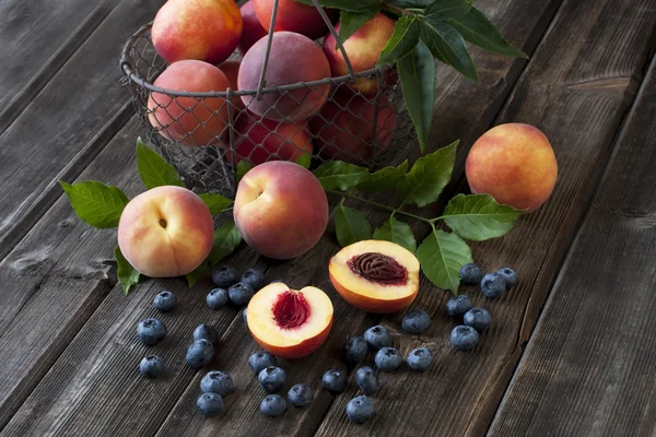 Verse perziken en nectarines met groene bladeren in een mand op een houten bord — Stockfoto