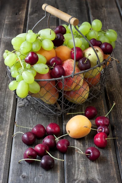 Natureza morta com frutas frescas em cesta de vime em mesa de madeira — Fotografia de Stock