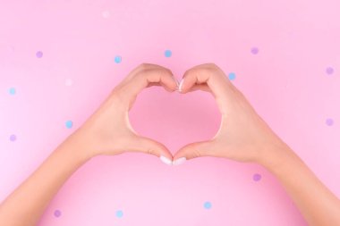 Güzel kadın, mükemmel manikürlü ellerdir. Pembe arka planda kalbi konfetiyle doldururlar. Düz yatış stili. Üst Manzara. Tasarım için yer.