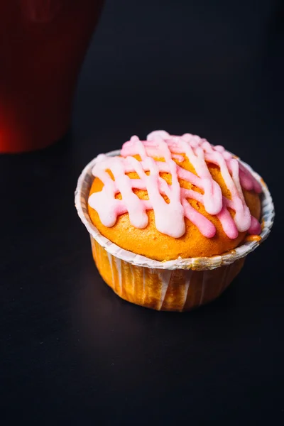 Cupcake with pink frosting and red cup on a wooden background — Stock Photo, Image