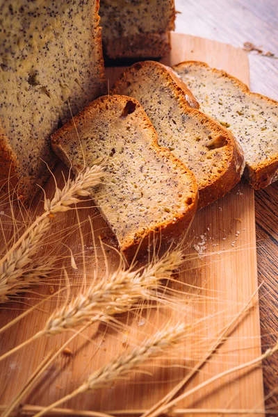 Закрыть ломтик свежего хлеба с семенами мака и колосьями пшеницы на деревянном фоне — стоковое фото