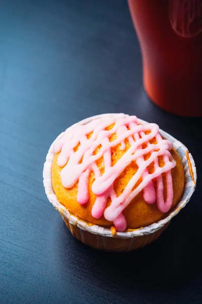 Кекс с розовой глазурью и красной чашкой на деревянном фоне — стоковое фото