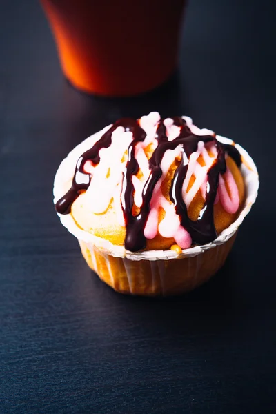 Cupcake mit rosa Zuckerguss und roter Tasse auf einem hölzernen Hintergrund — Stockfoto