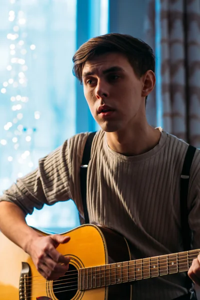 Young man sitting at home and playing guitar dramatic — Stock Photo, Image