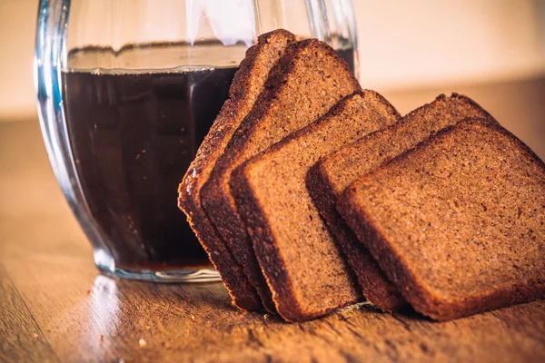 Russian brew in jug and loaf of rye flour on wooden background — Stock Photo, Image