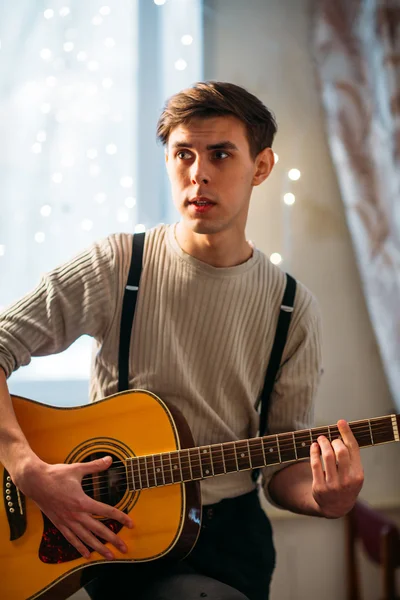 Young man sitting at home and playing guitar dramatic — Stock Photo, Image