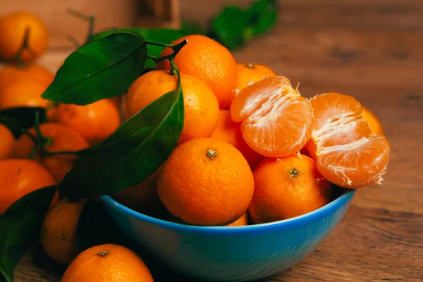 Багато свіжих мандаринських апельсинів у синій мисці, що стоять на дерев'яному столі — стокове фото