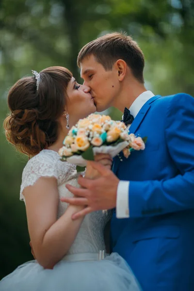 Mladá nevěsta a ženich líbat na pozadí lesa — Stock fotografie