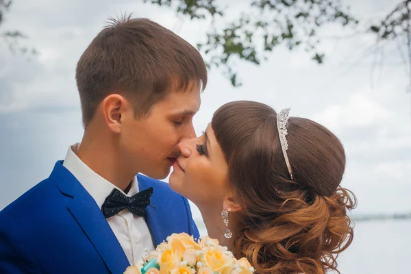 Braut und Bräutigam küssen sich auf dem Hintergrund von Bäumen — Stockfoto