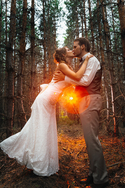 Dramatic picture bride and groom on the background of leaves and forest backlight.