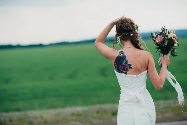 Noiva com tatuagens um buquê no campo verde — Fotografia de Stock