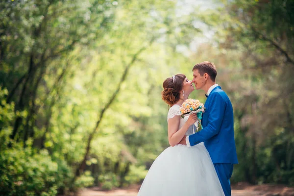Unga bruden och brudgummen embracing mot bakgrund av skogen vägen — Stockfoto