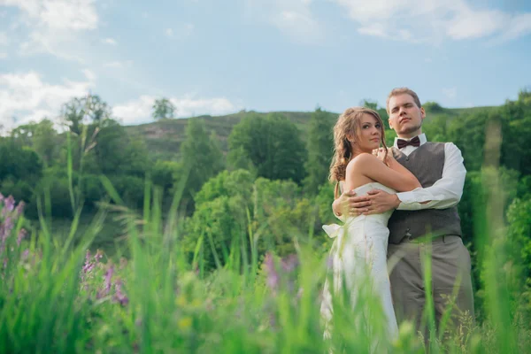 La mariée et le marié avec un bouquet dans l'herbe sur le fond paysage de montagne — Photo