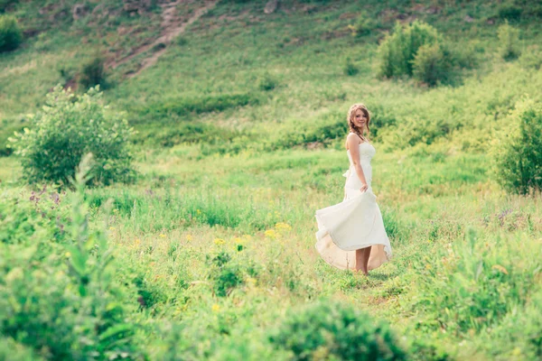 Bride stands on a background of grass and mountains — Stock Photo, Image