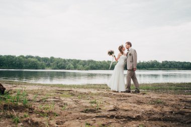 Genç damat ve gelin ayakta nehrin arka plan üzerinde sarılma.