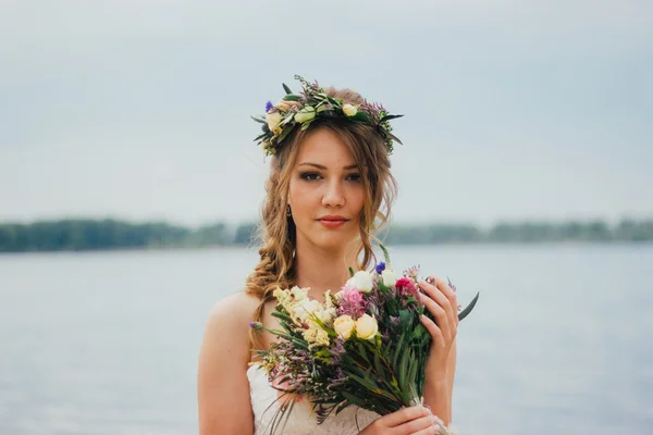 Jonge bruid met een boeket bloemen permanent op de achtergrond de rivier — Stockfoto