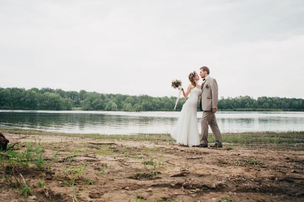 Young groom and bride standing hugging on the background of the river — Stock Photo, Image
