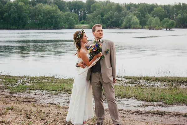 Young groom and bride standing hugging on the background of the river — Stock Photo, Image