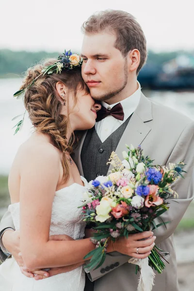 Unga brudgummen och bruden stående kramas på bakgrunden av floden — Stockfoto