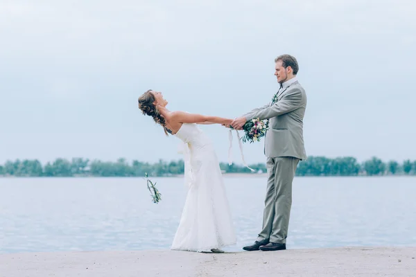 Young groom and bride standing hugging on the background of the river — Stock Photo, Image